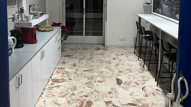 Une cuisine avec un sol en marbre, des meubles blancs, une machine à café et une horloge au mur.
