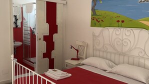 Une chambre avec un lit blanc, une literie rouge, un luminaire suspendu rouge, un tableau représentant un paysage et une tête de lit blanche.
