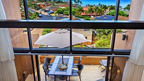 A balcony with a table and chairs, overlooking a residential area and the ocean. - Serenity framed by floor-to-ceiling Ocean views (Lahaina)