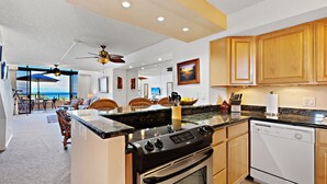 A kitchen with a stove, oven, and dishwasher, wooden cabinets, and a dining area with a view. - Serenity framed by floor-to-ceiling Ocean views (Lahaina)