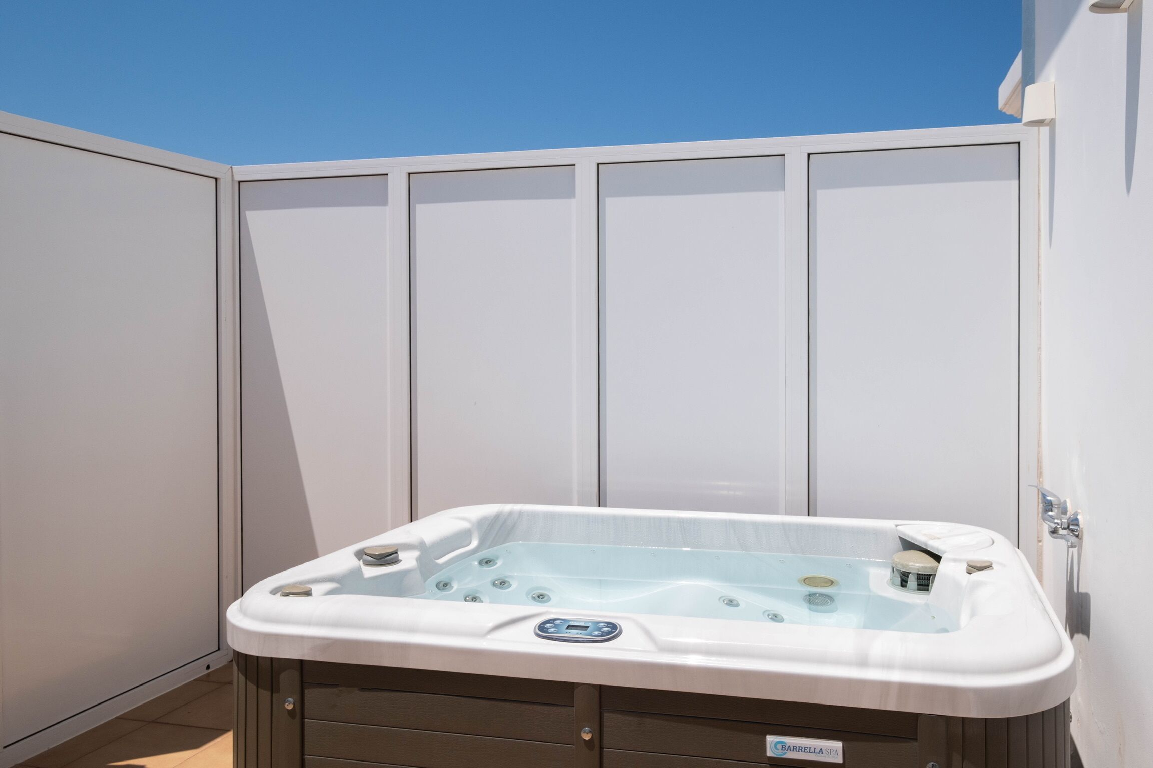 Ein Whirlpool im Spa-Bereich mit Bedienfeld, vor einer weißen Wand mit blauem Himmel.