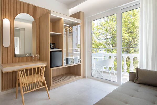 Una habitación moderna con tocador de madera, puerta de vidrio que da a un balcón exterior y un ventanal con vistas al exterior.