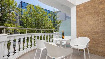 A balcony with white chairs, a table, and a bottle of wine.