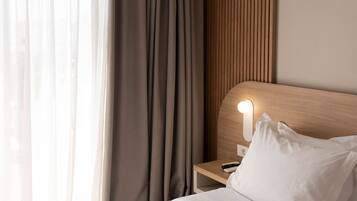 Une chambre d’hôtel avec un lit, une table de chevet, une lampe, une fenêtre avec des rideaux et un mur recouvert de panneaux de bois.