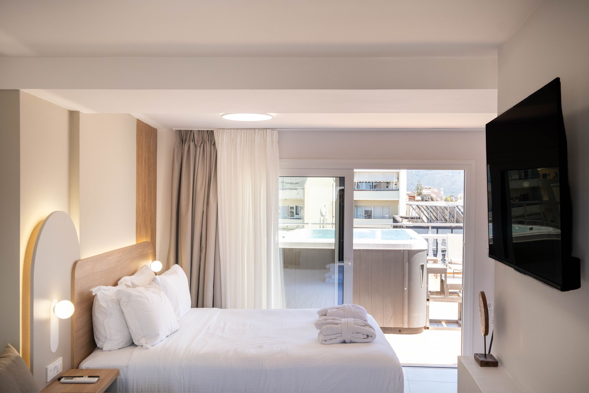 A hotel room with a bed, a TV mounted on the wall, and a view of a pool and outdoor seating area.