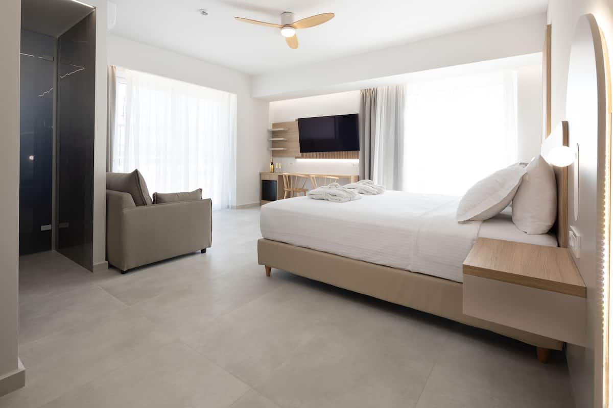 A modern hotel room with a large bed, a sofa, a TV, and a ceiling fan.