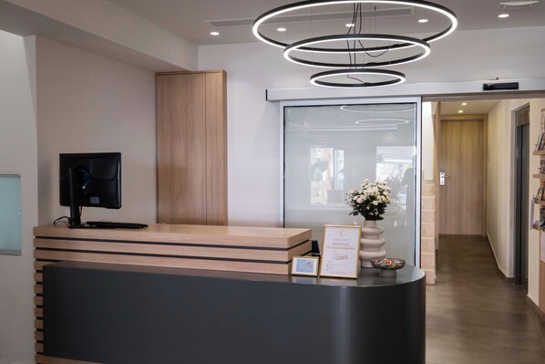 A reception desk with a flat-screen monitor, a framed certificate, and a vase of flowers. - Epavli Grace Hotel (Chania)