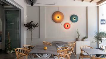 Un interior de cafetería moderno con mesas redondas, sillas de mimbre y luces decorativas en la pared.