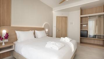 A modern hotel room with a large bed, a wooden headboard, a ceiling fan, a TV, and a wardrobe.