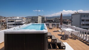Una terraza en la azotea con un jacuzzi, asientos al aire libre y vistas de la ciudad.