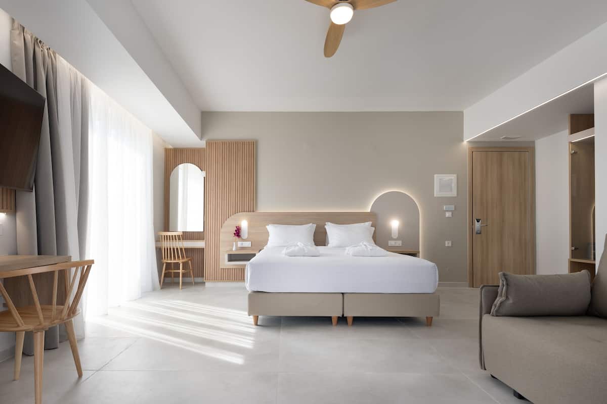 A modern hotel room with a large bed, a desk, and a sofa.