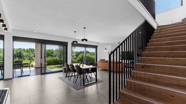A spacious living area with a dining table, chairs, and a sofa. A wooden staircase leads to an upper level. - Tola in Vi Njan With 3 Bedrooms and 3 Bathrooms (Visnjan)