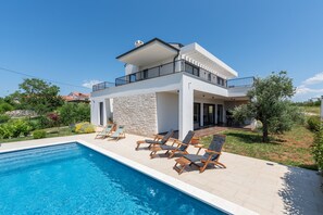 Ein modernes, zweistöckiges Haus mit Schwimmbad, Sitzgelegenheiten im Freien und einer Steinmauer.