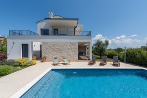Ein modernes, zweistöckiges Haus mit Pool, Sitzgelegenheit im Freien und einer Steinfassade.