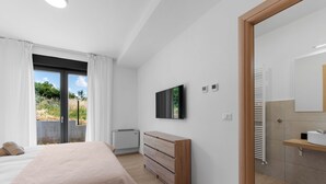 A modern bedroom with a large bed, a dresser, a television, and a bathroom with a mirror and towel rack. - Tola in Vi Njan With 3 Bedrooms and 3 Bathrooms (Visnjan)