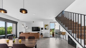 A modern living space with a dining area, a sofa, a staircase, and a TV. - Tola in Vi Njan With 3 Bedrooms and 3 Bathrooms (Visnjan)