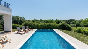 A rectangular swimming pool with clear blue water, surrounded by a tiled deck. There are several lounge chairs and a modern building with a balcony in the background. - Tola in Vi Njan With 3 Bedrooms and 3 Bathrooms (Visnjan)