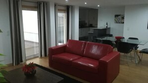 En moderne stue med en rød lædersofa, et glasbord med stole og et køkken i baggrunden.