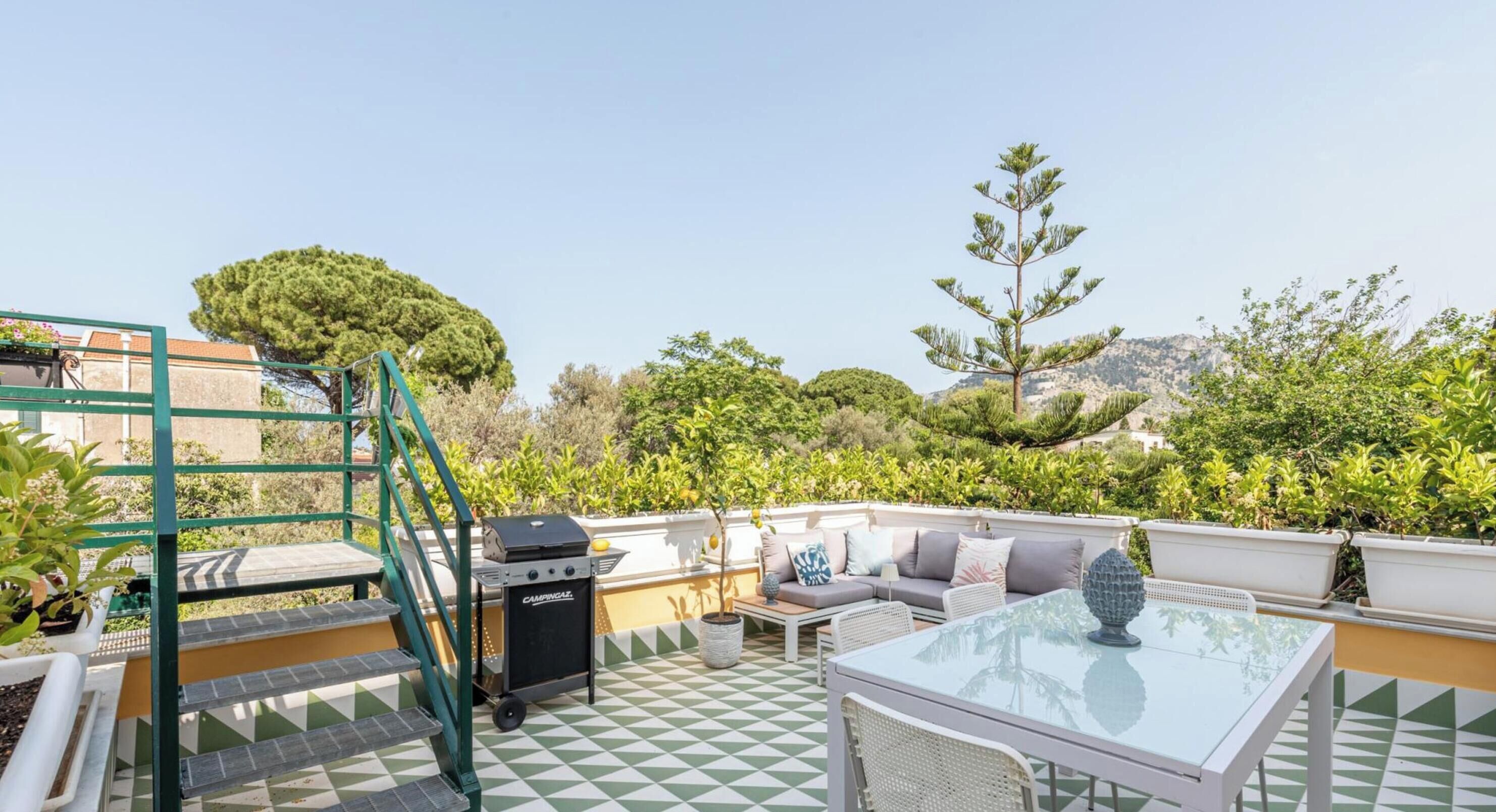 A rooftop terrace with a grill, seating area, and potted plants.