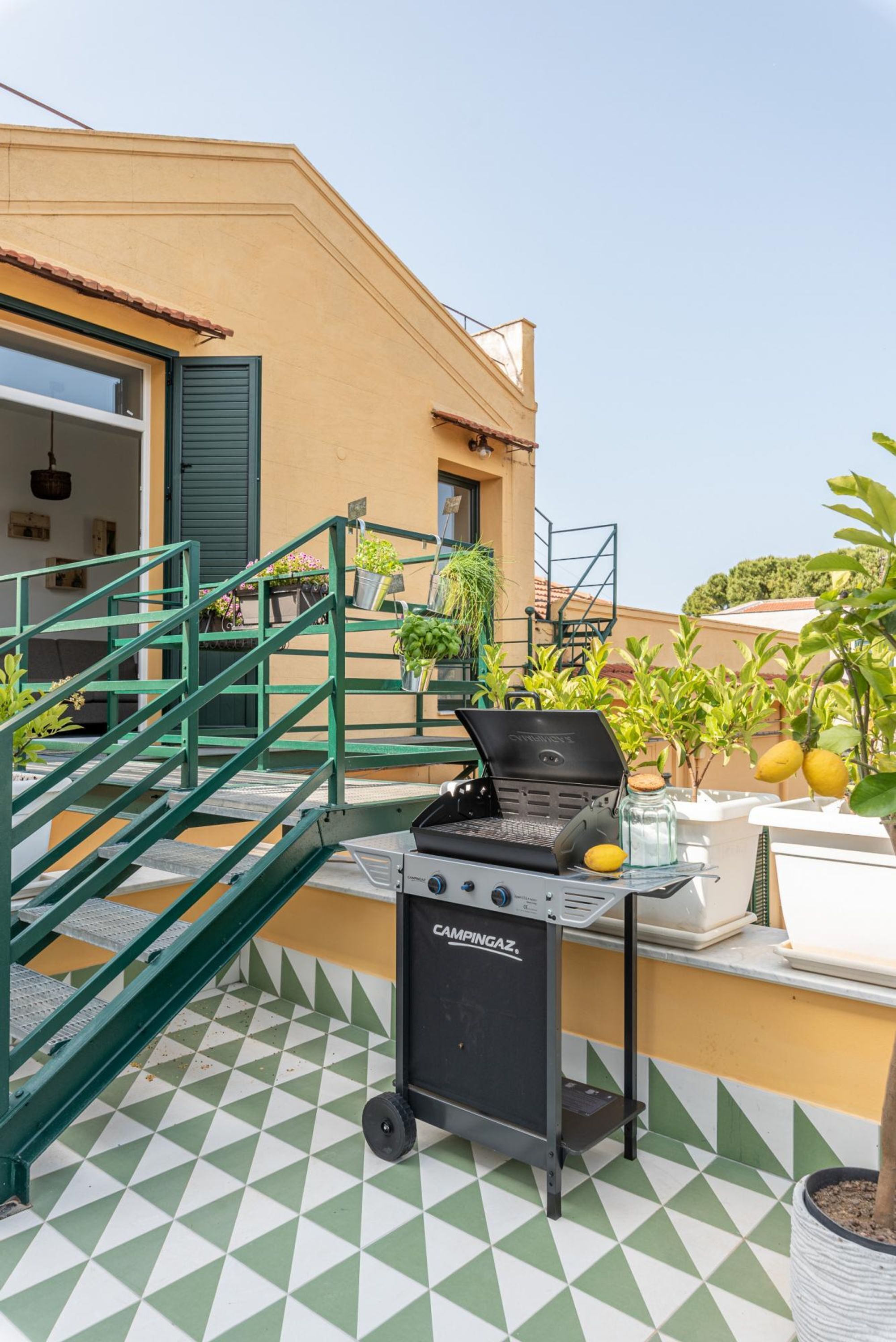 A rooftop terrace with a portable grill, potted plants, and a staircase.