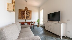 A living room with a sofa, a dining table with chairs, a TV on a cabinet, and a large painting on the wall.