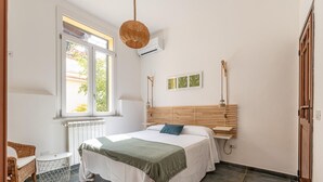 A bedroom with a bed, a window, a radiator, a hanging light fixture, and a wall-mounted shelf.