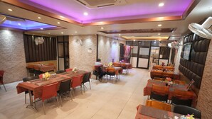 A restaurant with multiple tables and chairs, some with tablecloths, and a few with decorative centerpieces. - Hotel Raj Kamal Palace (Varanasi)