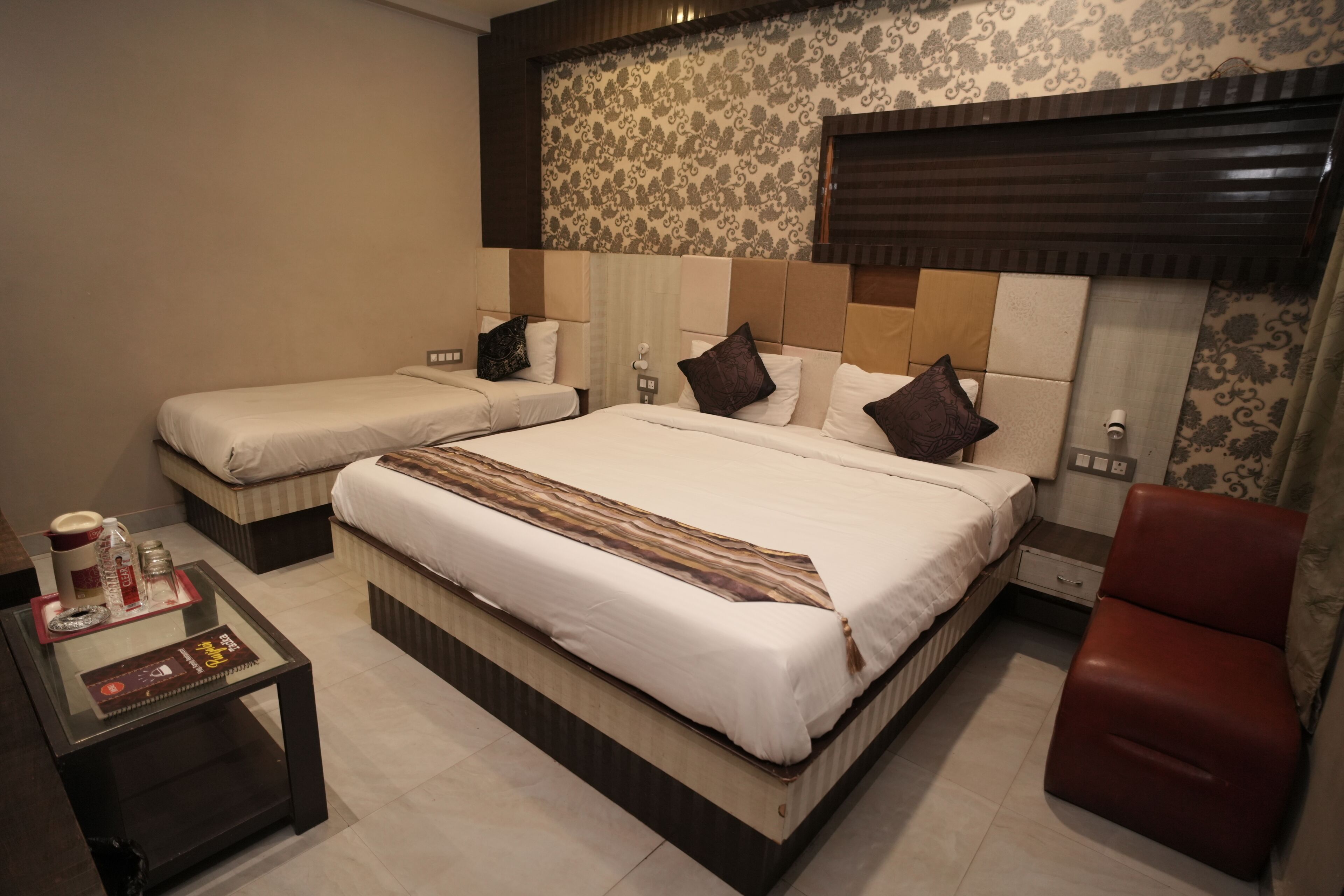 Habitación de hotel con dos camas, una mesita con bandeja y una silla roja.