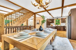 A dining area with a wooden table set for four, a staircase, and a kitchen in the background. - Brand New 4BR- fire pit, hot tub, game room. (Bethel)