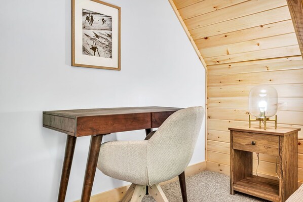 A cozy room with a wooden desk, a chair, a small bedside table with a lamp, and a framed picture on the wall. - Brand New 4BR- fire pit, hot tub, game room. (Bethel)