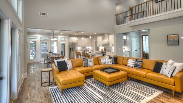 A spacious living area with a large sectional sofa, a coffee table, and a striped rug. There is a staircase leading to an upper level with a railing.