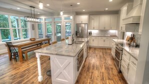 A spacious kitchen with wooden flooring, white cabinetry, and a large island with a sink.