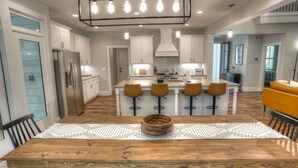 A modern kitchen with white cabinets, a central island with stools, and a wooden dining table.
