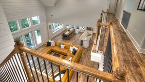 A spacious loft-style living area with a high ceiling, large windows, and a wooden staircase.