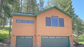 A two-story log cabin with two green garage doors and a small porch. - Lariat Bunkhouse (Rapid City)