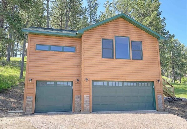 A two-story log cabin with two green garage doors and a small porch.