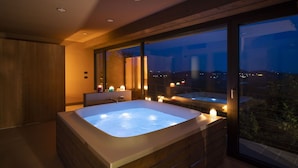Ein modernes Badezimmer mit einer großen Badewanne, Holzschränken und Blick auf die Stadt im Abendrot.