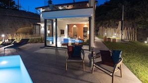Ein Außenbereich mit einer patioartigen Terrasse, einem mit Glas geschlossenen Essbereich, Sitzgelegenheiten im Freien und einem Pool.