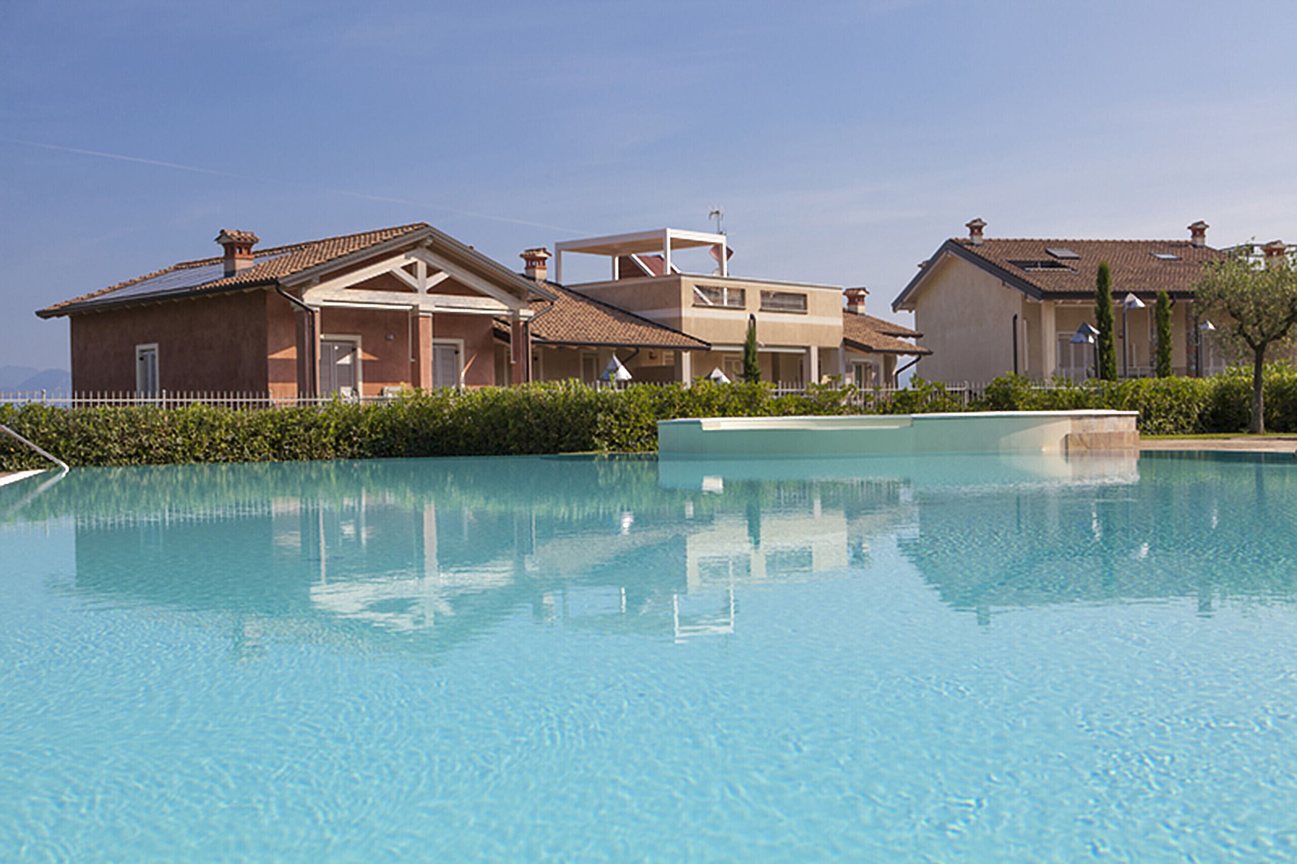 Ein Swimmingpool mit einer klaren, blauen Wasseroberfläche, umgeben von einem weißen Zaun und üppigem Grün.