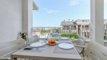 Un balcon avec une table dressée pour deux personnes, comprenant des assiettes, des couverts et un panier de fruits.