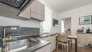A modern kitchen with a stainless steel sink, wooden cabinets, and a dining area with a table and chairs.