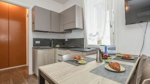 A modern kitchen with a dining area, featuring a wooden table set for breakfast with croissants and a coffee cup.