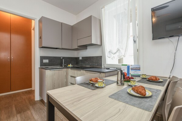 A compact kitchen with a dining area, a television mounted on the wall, and a table set for breakfast.