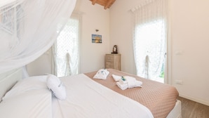 A neatly made bed with a white and pink bedspread, a wooden nightstand with a mirror, and a small painting on the wall.