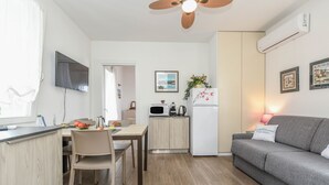 A modern kitchen with a dining area, a grey sofa, and a ceiling fan.