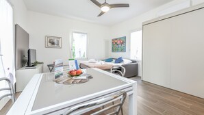 A modern living room with a dining area, a sofa, a ceiling fan, and a large window.