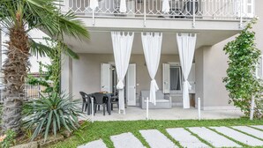 A balcony with white curtains, a table with chairs, and a palm tree.