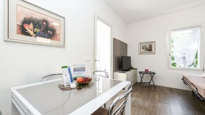 A modern room with a glass dining table, a flat-screen TV, and a bed with a window view.