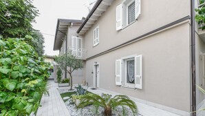 A residential building with a paved walkway, white shutters, and a small garden area with gravel and plants.