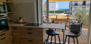A kitchen with a marble countertop, a stove, and a window overlooking a balcony with outdoor furniture. - Duplex Avec Jardin, Piscine, Terrasse, 3 Chambres (Palavas-les-Flots)